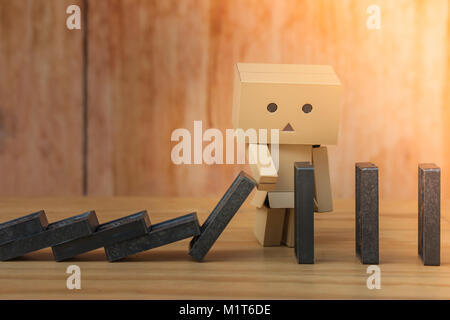 Business Dominos Effect Concept : Paper doll halting or stopping domino falling effect from continuous topple with hand on wooden floor. Stock Photo