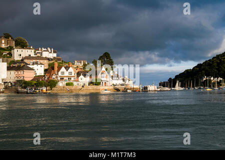 Sunlit Kingswear under Dark Skies: View from the River Dart looking Towards Kingswear, the Sea and Dartmouth Castle. Kingswear, Devon, England. Stock Photo