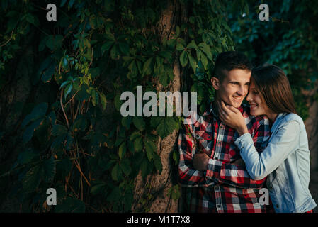 Close-up portrait of the cheerful smiling young couple near the wall overgrown with plants. The girl is stroking the face of the man. Wroclaw, Poland, Centennial Hall location. Stock Photo