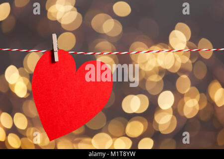 Red paper heart shape pegged to a string with blurred bokeh lights in the background Stock Photo