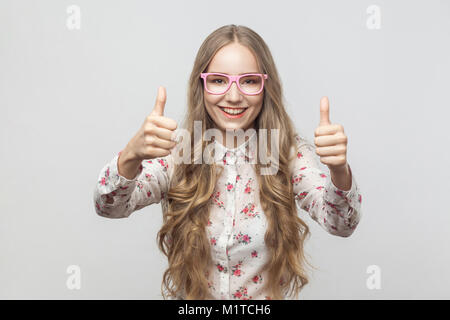 Happiness  blonde girl in sunglasses, showing thumbs up, looking at camera and smiling. Studio shot. Isolated on gray background Stock Photo