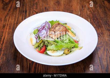 Nicoise salad in a plate on the table. In the plate is tuna, eggs, asparagus, lettuce, olives, onions,  tomatoes, spices Stock Photo