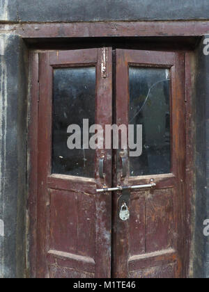 Old wooden doors are dark brown with dark glasses on the black wall. Stock Photo