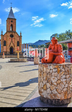 BOYACA, COLOMBIA - JANUARY 23, 2014: A beautiful ceramic sculpture of a craftsman in the foreground and the church in the background in the main squar Stock Photo