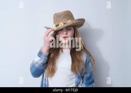 Girl with eyes closed in blue plaid shirt and straw hat with white daisies on white background Stock Photo