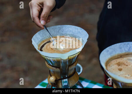 Barista stirs pour over coffee in artisan glass brewer while outdoors Stock Photo
