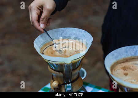Barista stirs pour over coffee in artisan glass brewer while outdoors Stock Photo