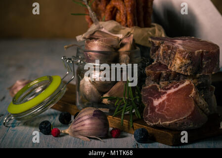 Horizontal photo of tuscany wild boar meat which is dried and smoked. Meat is cut to pieces and stacked on wooden board with sausages in can, garlic i Stock Photo