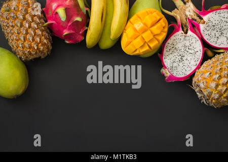 Tropical fruits pineapple, banana, dragon fruit and mango on black background. Top view. Copy space. Stock Photo