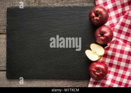 Ripe red apples on wooden board with red checkered napkin around and copy space on black slate dish. Stock Photo