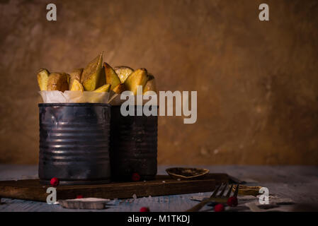 Horizontal photo with two vintage cans with worn surface full of roasted potato strips. Potatoes are un-peeled and fried with skin. Cans are on vintag Stock Photo