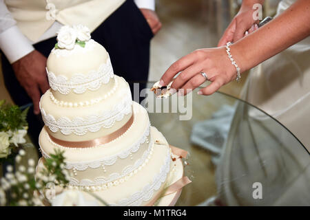 Wedding couple cut into their wedding cake taking a small slice, hands only on show.UK Stock Photo
