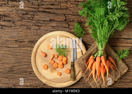 Fresh organic sliced carrots with green leaves on old wood background and top view. Vegetables. Healthy food Stock Photo