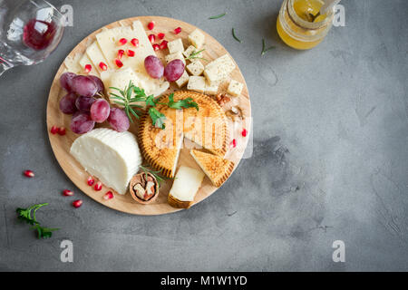 Cheese platter with assorted cheeses, grapes, nuts over gray stone background, copy space. Italian cheese and fruit platter. Stock Photo