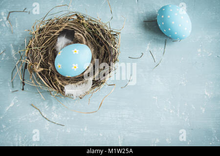 Easter Eggs in bird Nest on blue wooden background. Decorated easter eggs with feathers in nest on old wooden table with copy space. Spring, Easter or Stock Photo