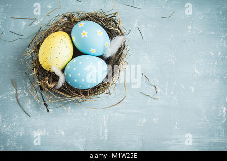 Easter Eggs in bird Nest on blue wooden background. Decorated easter eggs with feathers in nest on old wooden table with copy space. Spring, Easter or Stock Photo