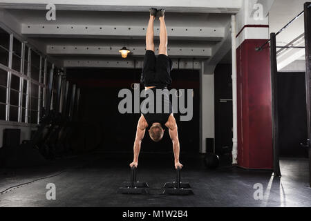 Young Athlete Man Doing Handstand Exercise On Parallel Bar In The Gym Stock Photo