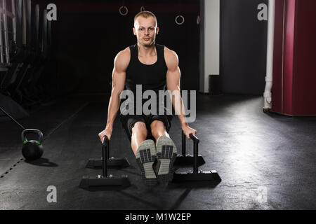 Portrait Of A Young Man Doing Push-up Exercise On Push-up Bar In The Gym Stock Photo