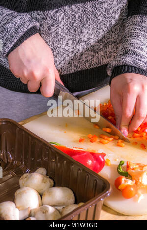 A woman (hands only) chopping a red pepper with a large, sharp, stainless steel kitchen knife. on a plastic chopping board. UK. Stock Photo