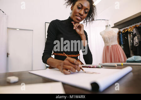 Female fashion entrepreneur making a drawing in her cloth workshop. Fashion designer sketching a design sitting at her table.