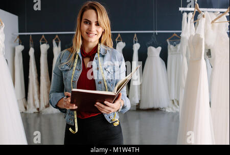 Portrait of happy young female bridal store owner with a diary. Woman tailor working in bridal boutique. Stock Photo