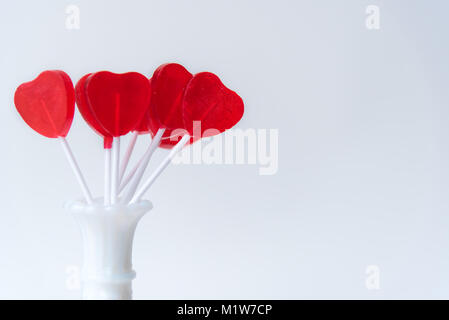 Cute red heart-shaped lollipops displayed in white vase against white background Stock Photo