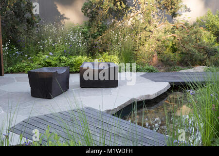 modern garden with stone paving paved patio area wooden decking small pond Chelsea Flower Show UK wooden walkway over pool, charred wooden cube seat Stock Photo