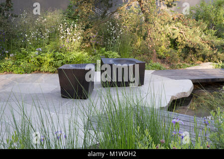 modern garden with wooden cube seats stone patio paving paved Chelsea Flower Show wooden deck decking walkway over small water feature pool pond Stock Photo