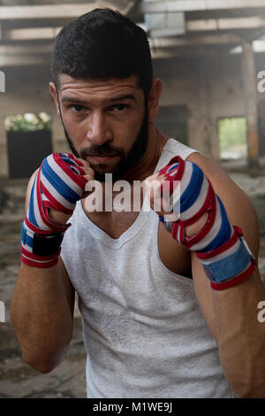 Portrait of muscular male boxer posing in boxing stance inside abandoned building. Stock Photo