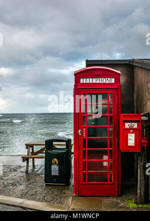 Pennan, Aberdeenshire, Scotland, United Kingdom. The strong winds create a surge in the North Sea along the Northeast coast of Scotland, with large waves splashing against the promenade in the picturesque village, famous for being a film location for the movie Local Hero. The iconic British red telephone box, originally a film prop, was installed afterwards as a result of public demand Stock Photo