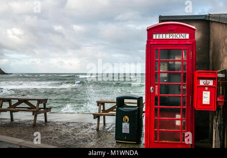 Pennan, Aberdeenshire, Scotland, United Kingdom. The strong winds create a surge in the North Sea along the Northeast coast of Scotland, with large waves splashing against the promenade in the picturesque village, famous for being a film location for the movie Local Hero. The iconic British red telephone box, originally a film prop, was installed afterwards as a result of public demand Stock Photo