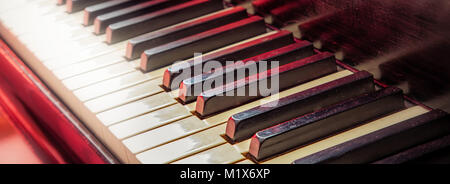 The keys of a piano with a red light in the background. Stock Photo