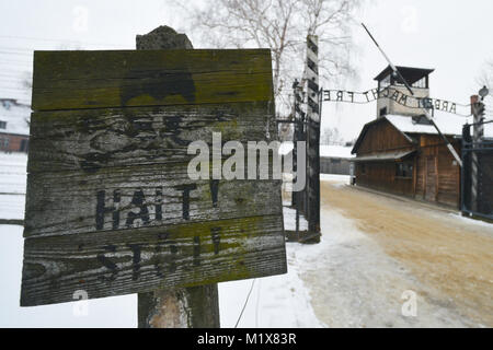 Halt sign near Arbeit Macht Frei (English: work sets you free) sign at the entrance near barbed wire fences and barriers inside Auschwitz I German Naz Stock Photo
