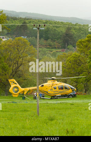 An Air Ambulance lands and takes off from a field near trees and power lines, attending an injured person. Stock Photo