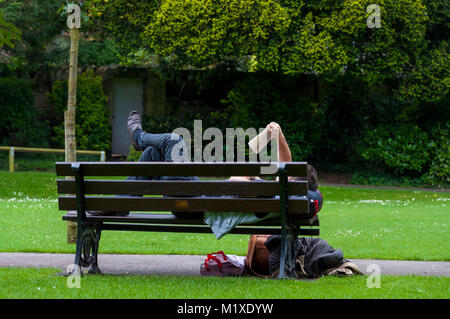 Man reads a book on a park bench in Henrietta Park, Bath, UK Stock Photo