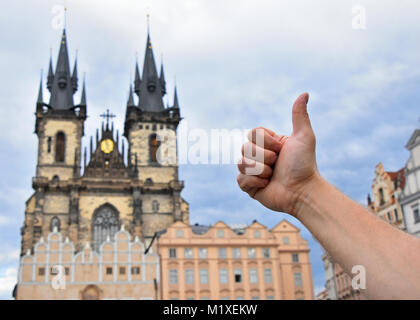 Close up man hand showing thumb up gesture over cityscape with Cathedral of Our Lady before Tyn, Prague, Czech Republic Stock Photo