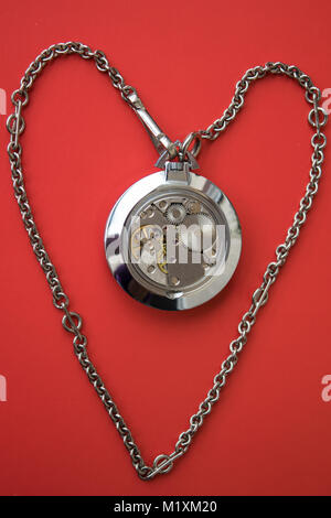 Clockwork Mechanism of Old Silver Pocket Watch with Heart shaped chain on red background Stock Photo