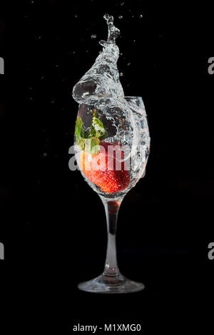 Strawberry dropped into wine glass, water splashing frozen in motion. Stock Photo