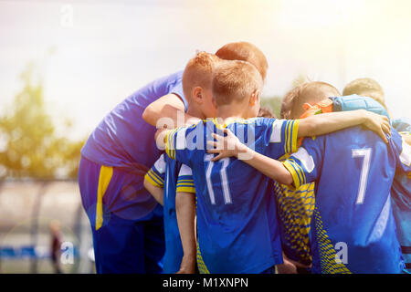 Kids sport team having pep talk with coach. Children soccer team motivated by trainer. Coaching football youth team. Young boys standing together unit Stock Photo