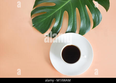 Cup of coffee and green big leaf Monstera plant on pink background. Concept and top view. Stock Photo