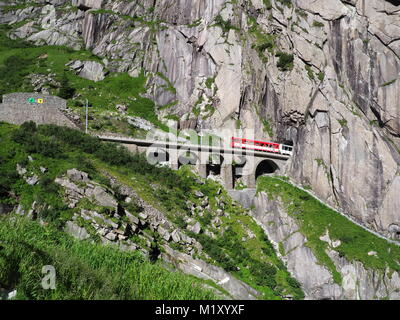 Express St. Gotthard train on Teufelsbruecke near Andermatt in Switzerland, Devil's railway bridge and tunnel, swiss Alps, alpine rocky mountains. Stock Photo