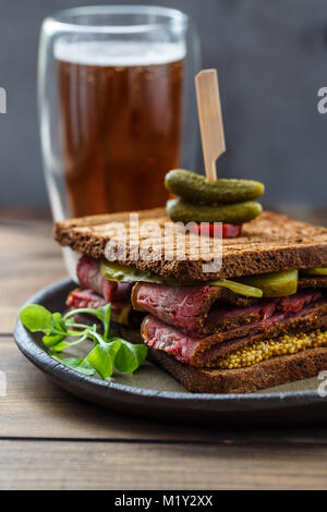 Pastrami sandwich with mustard and pickle with beer on wooden background Stock Photo