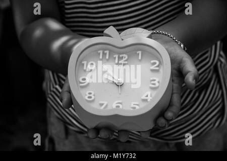 Abstract black and white image image of cute girl holding and showing blue alarm clock in her hand in vintage style. Stock Photo