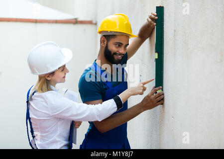 Smiling blonde female engineer and black specialist checking wall plane Stock Photo