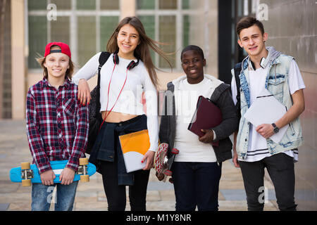 Ordinary four friends with folders and backpacks near college Stock Photo