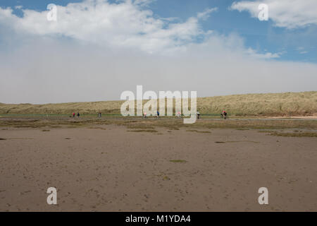 Walkers and cyclists crossing the causeway from Lindisfarne to the mainland on a sunny day Stock Photo