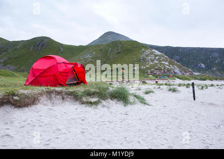 Red tent on green grass near the sand at Haukland Beach, Lofoten Islands, Norway.