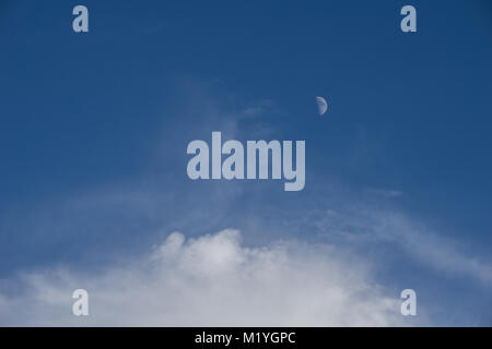 The moon out in the middle of the day and white fluffy clouds Stock Photo