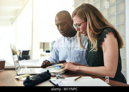 Two designers choosing color swatches while working together at a table in a modern office Stock Photo