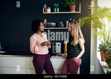 Two diverse female work colleagues smiling and talking together while taking a break in a modern office Stock Photo